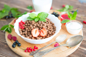 Bowl of healthy corn flakes breakfast cereal topped with fresh blackcurrants and strawberries served in a white ceramic bowl for a delicious meal Healthy tasty breakfast chocolate balls.