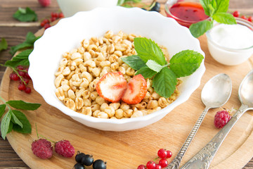 Healthy breakfast with corn flakes, berries, waffle and milk on blue background. Close up. Healthy tasty breakfast of muesli with strawberries, raspberries, black currants and red currants.