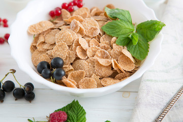 Healthy breakfast with cornflakes and fresh berries on white wooden Healthy tasty breakfast multigrain wholewheat healthy cereals with strawberries, raspberries, black currants and red currants.