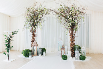 Indoor wedding ceremony with white wedding arch decorated with flowers and big white candles