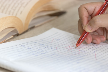 Concept of measurement and evaluation. Hand of teacher using red pen written grade A and circle on math exam paper on wood desk and book opened  nearby.