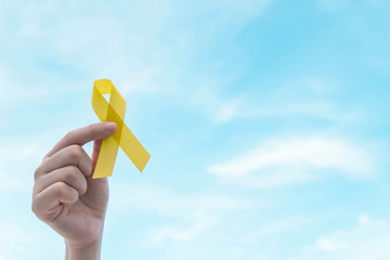 Hand holding yellow gold ribbon awareness over blue sky. Symbol for support suicide prevention,...
