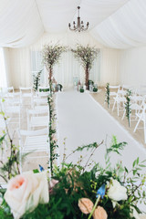 Indoor wedding ceremony with white wedding arch decorated with flowers and big white candles