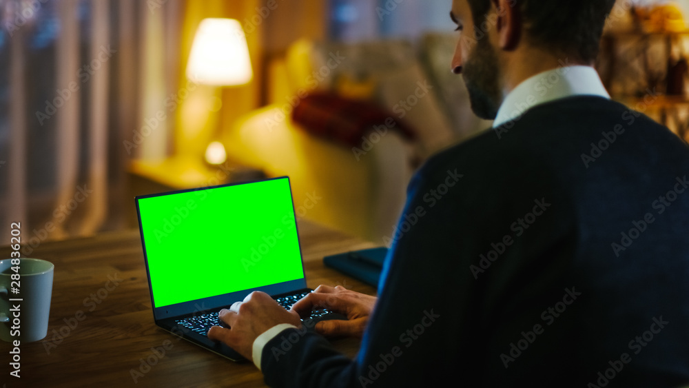 Aufkleber at home back view of a man sitting at his desk and typing on a laptop with green screen on it. his a
