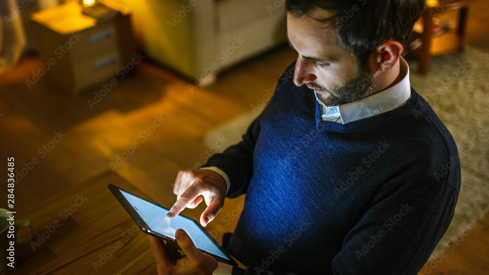 Poster respectable middle aged man sitting at his desk using tablet computer. he's at home alone. in the ba
