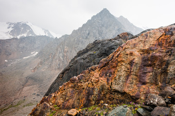 Bright large red stone with purple streaks. A pyramid-shaped mountain and a mountain peak in snow and a glacier. Gigantic sticking out stone. Mountain valley of Altai nature. An admixture of iron ore 