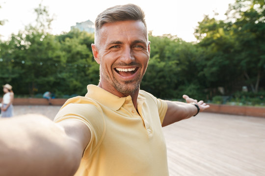 Image closeup of happy middle-aged man taking selfie photo and laughing while walking in summer park