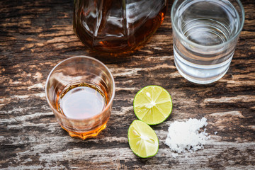 alcoholic drinks and lemon salt on rustic wood background - brandy in a glass with alcohol bottles...