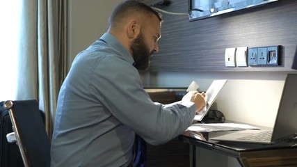 Businessman working with tablet and documents at hotel room - Powered by Adobe