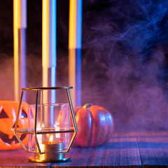 Halloween concept, orange pumpkin lantern and candles on a dark wooden table with blue-orange smoke around the background, trick or treat, close up