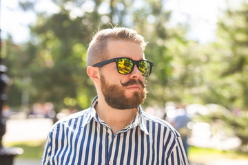 Portrait of a positive cheerful young man walking in the park on a warm sunny summer day. The concept of rest after study and work on weekends.