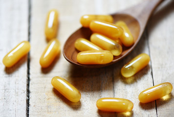 Royal jelly capsules in wooden spoon and wood table background - Yellow capsule medicine or supplementary food from nature for health