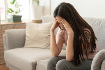 Asian woman are holding their hands to the head in pain on the sofa at home, Young women have severe headaches from migraines, Health and illness concept - 284840892