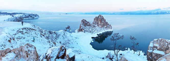 Baikal Lake at December morning. Panoramic view from Cape Burhan on a natural landmark Shamanka Rock after a snowfall. Photographer with a tripod takes a winter landscape