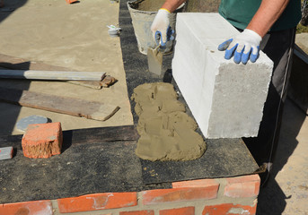Bricklayer builder laying autoclaved aerated concrete blocks for house foundation wall with waterproofing bitumen membrane