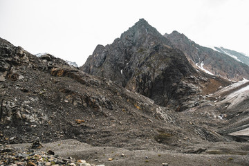 The slopes of high snowy mountain ranges. An embankment of many small stones. Beautiful views of difficult to climb, sharp mountains in a tourist trip through the nature of Altai land. Aktru Glacier.