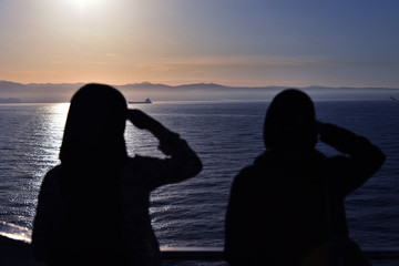 Back of two ladies watching and taking photograph of sunset by the fence of sea cruise. Two girls look at yachts that float on the river. Two happy female  friends on a cruise ship.
