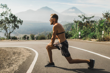 Runner doing lunges and warming-up before running on the road. Summer weather, topless body and sunglasses.