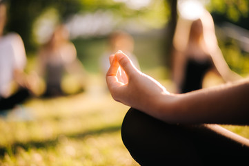 Close-up of hand of young yogi woman sitting in lotus pose in city park on sunny summer morning at...