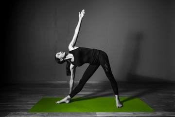 Black white photo of Young beautiful woman brunette in black clothes practice yoga utthita trikonasana in dark studio green mat Sport meditation monochrome