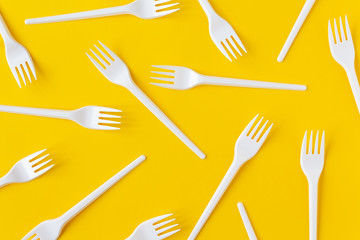 White plastic forks on yellow background. Flatlay.