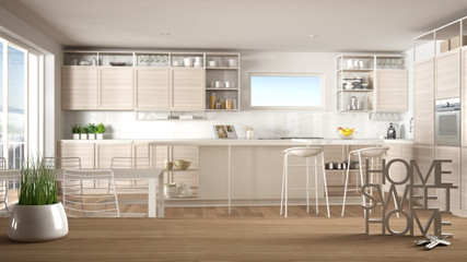 Wooden table, desk or shelf with potted grass plant, house keys and 3D letters making the words home sweet home, over modern white kitchen, interior design, blur background