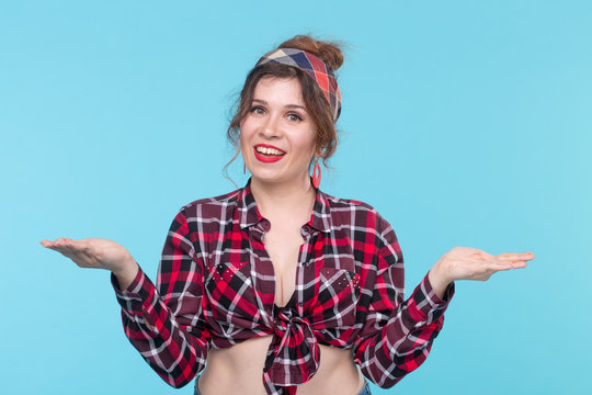 Nice young positive woman in plaid shirt posing over blue background with arms spread to the side. Concept of choice and suggestion.