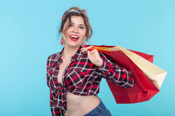 Happy young beautiful woman in a plaid shirt and jeans and holding a bag on a blue background....