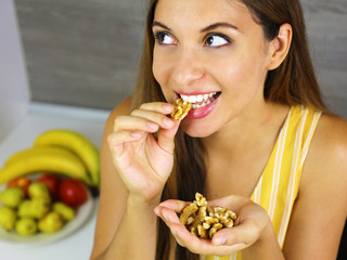 Beautiful young woman smiling and eating walnuts at home. Close up from above looking to the side.