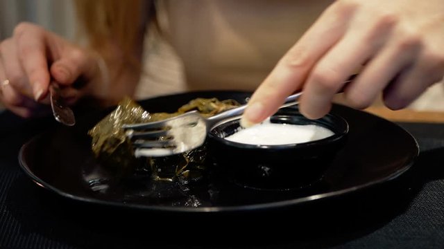 National traditional cuisine food in the restaurant. Woman is eating traditional georgian dolma with sour cream served in clay plate, dish closeup. Girl is eating with fork and knife