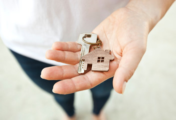 The mental key from door with wooden trinket in shape of house in woman's hand