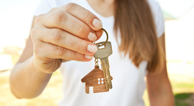 The mental key from door with wooden trinket in shape of house in woman's hand