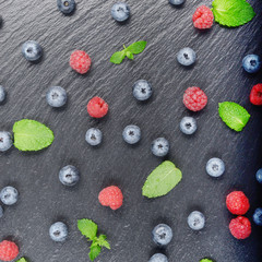 Flat lay view at ripe bilberry and raspberry berries on slate stone tray closeup