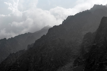 Mountain Altai. Mountain peaks in the misty clouds. Sunlight through the clouds. Beautiful views of high, sharp mountains in a tourist trip through the nature of Altai land.