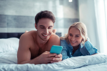 Couple laughing while watching funny video chilling in bed