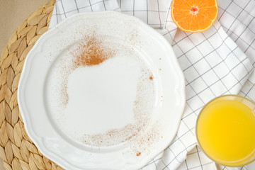 an empty plate sprinkled with cinnamon, a glass of orange juice and half a tangerine