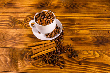 White cup filled with coffee beans, star anise and cinnamon sticks on wooden table