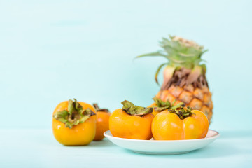 Fresh persimmon and pineapple on pastel background