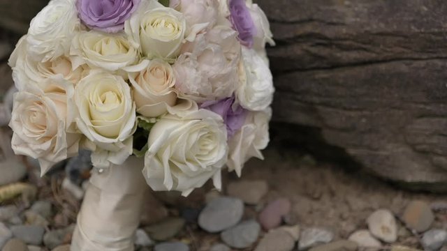 Close up tilt up on bride’s bouquet outside on rocks