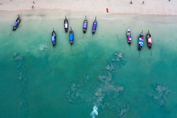 Aerial view of traditional longtail boats floating on a turquoise and clear ocean in Thailand.
