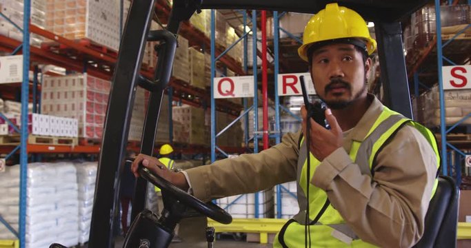 Young man working in a warehouse sitting in a forklift truck 4k