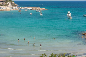 Fototapeta na wymiar Orihuela Costa, Spain - June 16, 2018: People sunbathing and swiming at the Cala Capitan beach in the Cabo Roig, popular place for holidaymakers. Province of Alicante. Costa Blanca. Spain