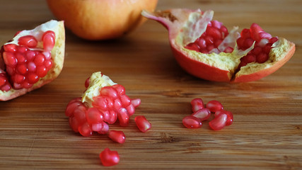 Open pomegranate or Punica granatum, popular fruit for multiple health benefits, revealing white fibrous arils and thick, waxy peel, with focus on clusters of red, juicy seeds spread on a wooden board