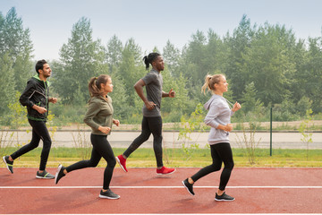 Side view of four young sportsmen and sportswomen running down racetracks