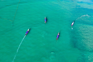 Aerial view of traditional longtail boats floating on a turquoise and clear ocean in Thailand.