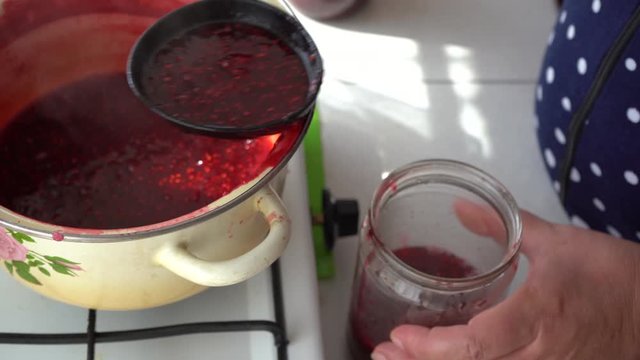 Woman puts handmade berry jam in jar. Boil raspberry jam. Vibrant colors in sunlight.