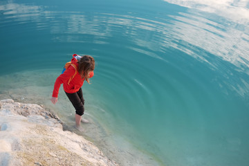 Fototapeta premium Barefoot caucasian kid weared in red hoodie plays in blue sea water