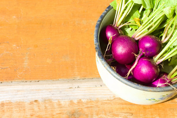Harvest of purple radishes in a metal bowl on a wooden table