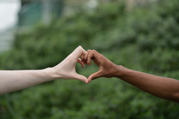 Light and dark-skinned men making heart with hands