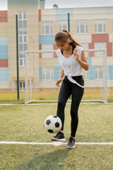 Fit girl in sportswear standing on sports field while kicking soccer ball © pressmaster